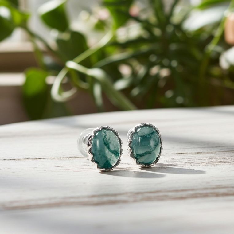 moss agate earrings on a wooden surface with plants in the background